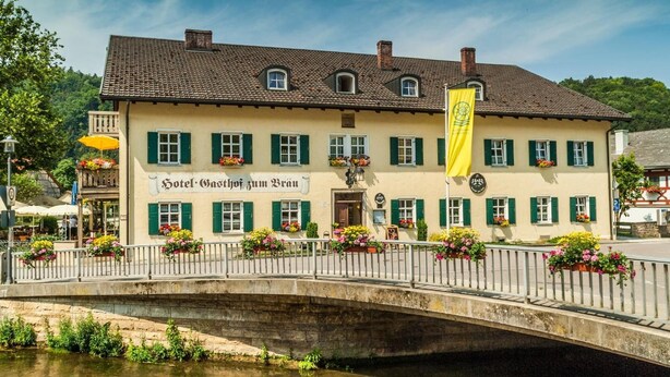 Il s'agit d'un bâtiment traditionnel sur lequel on peut lire l'inscription « Hôtel Gasthof zum Brun ». On y trouve un pont enjambant un plan d'eau, des volets verts et des jardinières fleuries.