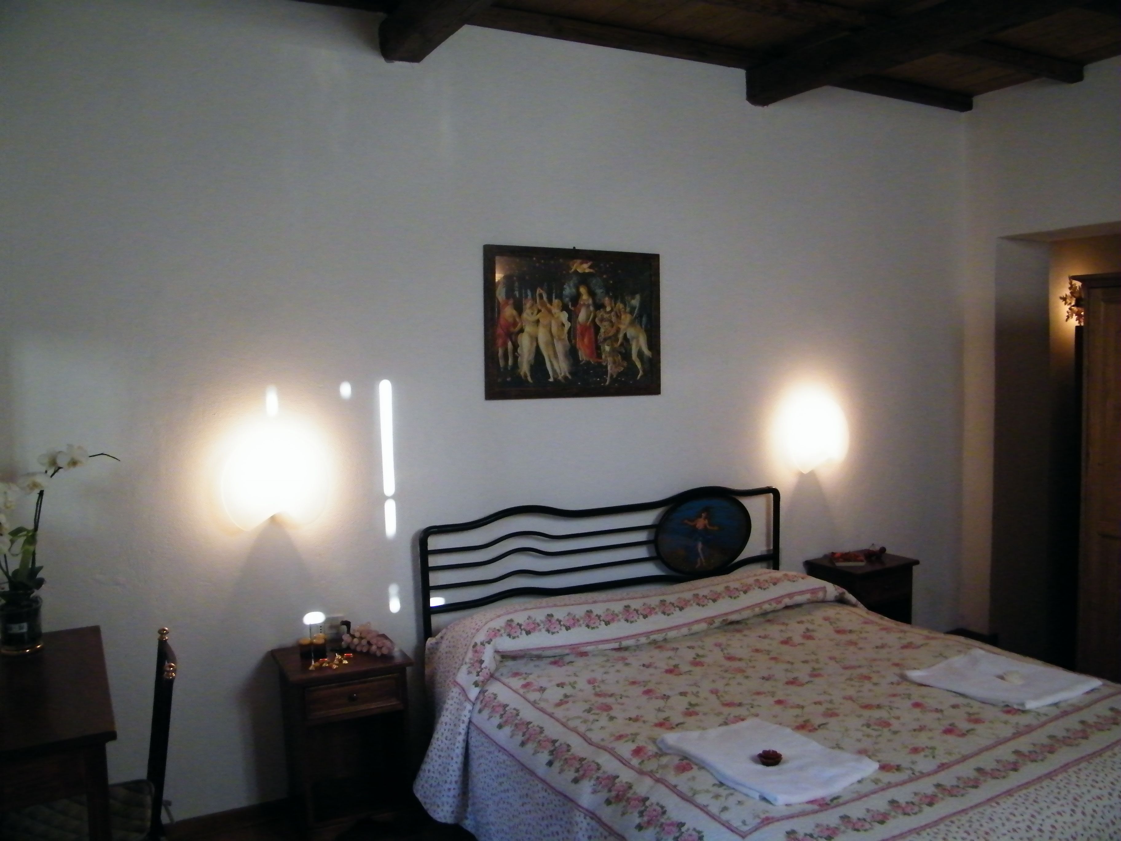 Ein Schlafzimmer mit einem Bett, einem Nachttisch, einem Wandbild und zwei Wandleuchten.