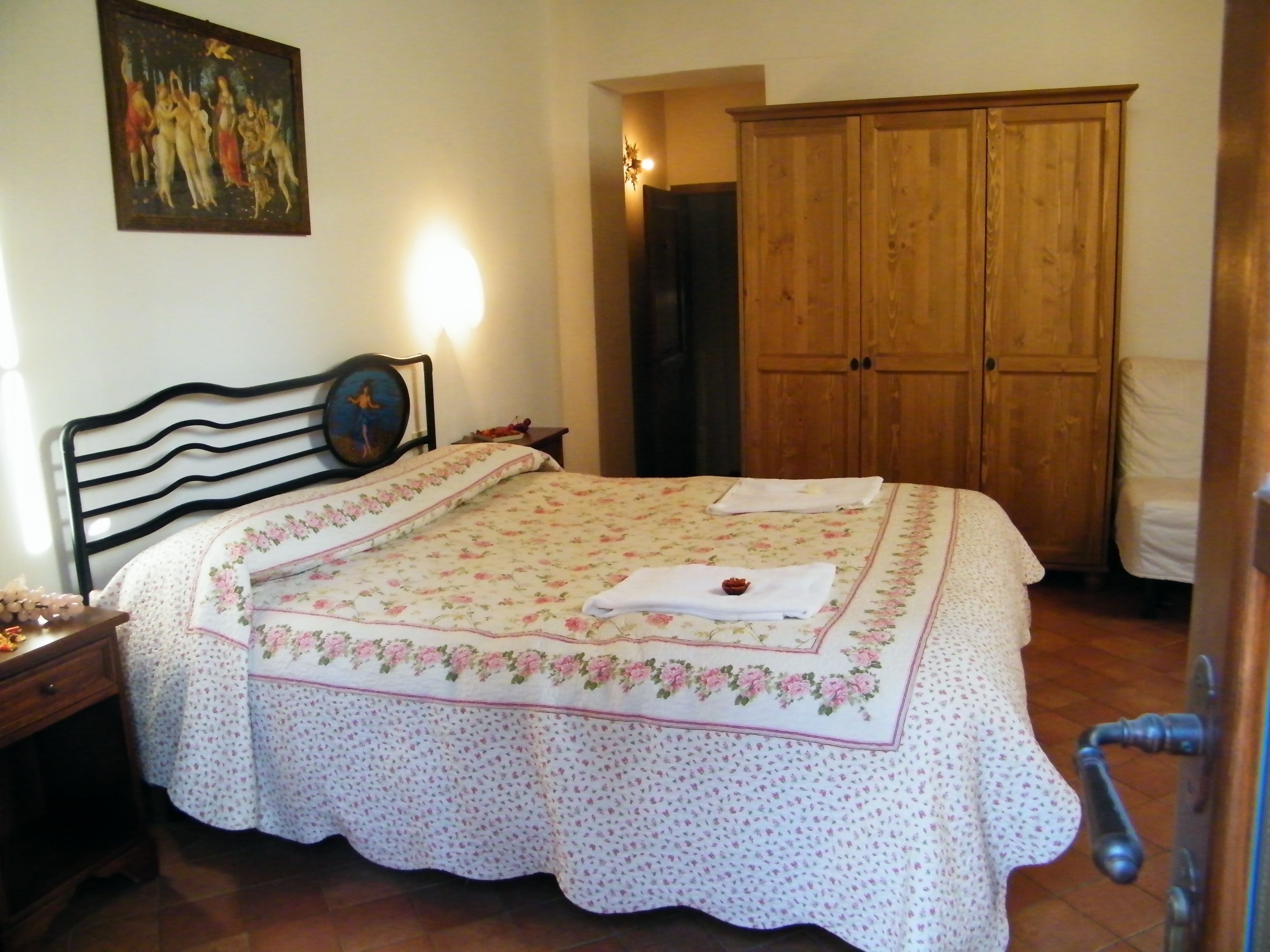 Ein Schlafzimmer mit Bett, Holzschrank, Nachttisch, einem Bild an der Wand und einer Tür zu einem anderen Raum.