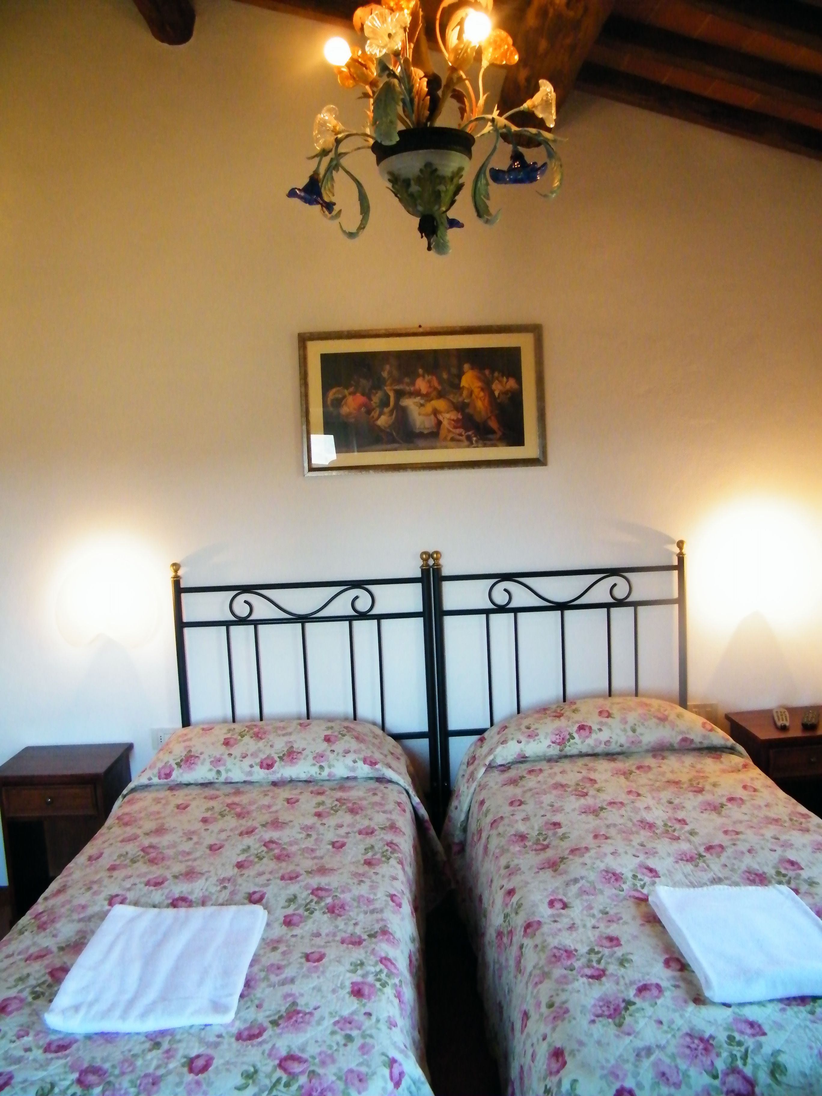 A room with two beds, a chandelier, a framed painting, and a nightstand with a remote control.