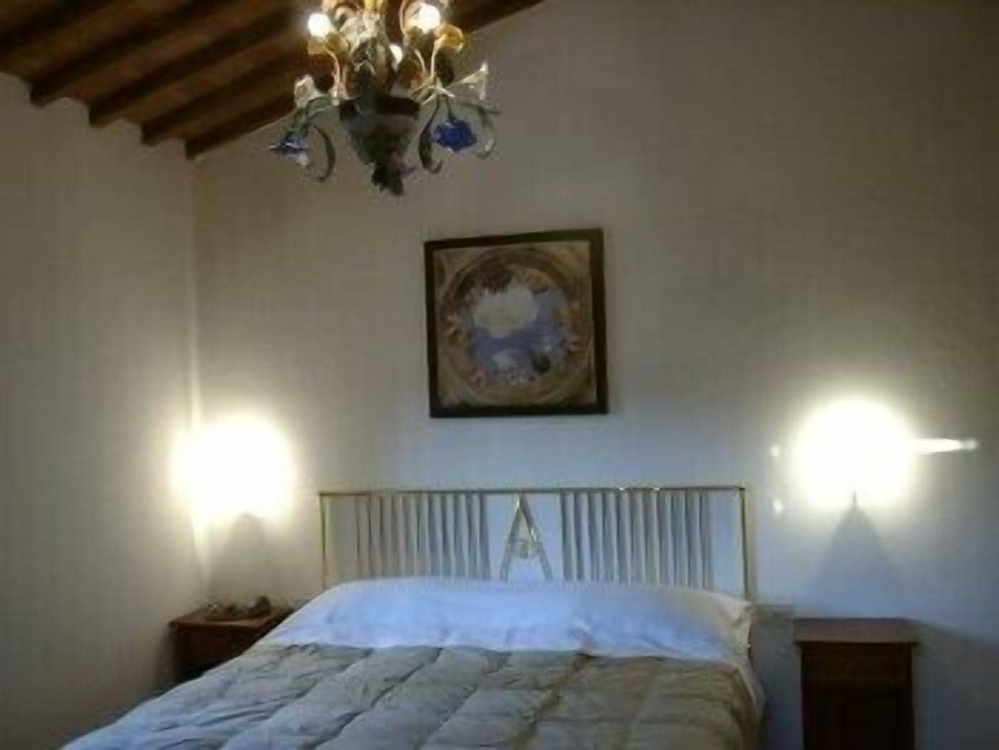Quarto com cama, lustre, pintura e duas luzes fixadas na parede.