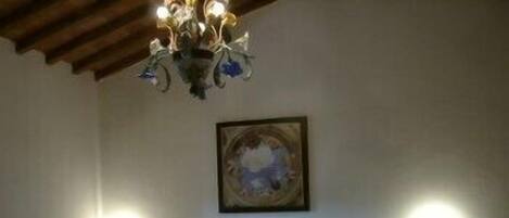 Quarto com cama, lustre, pintura e duas luzes fixadas na parede.