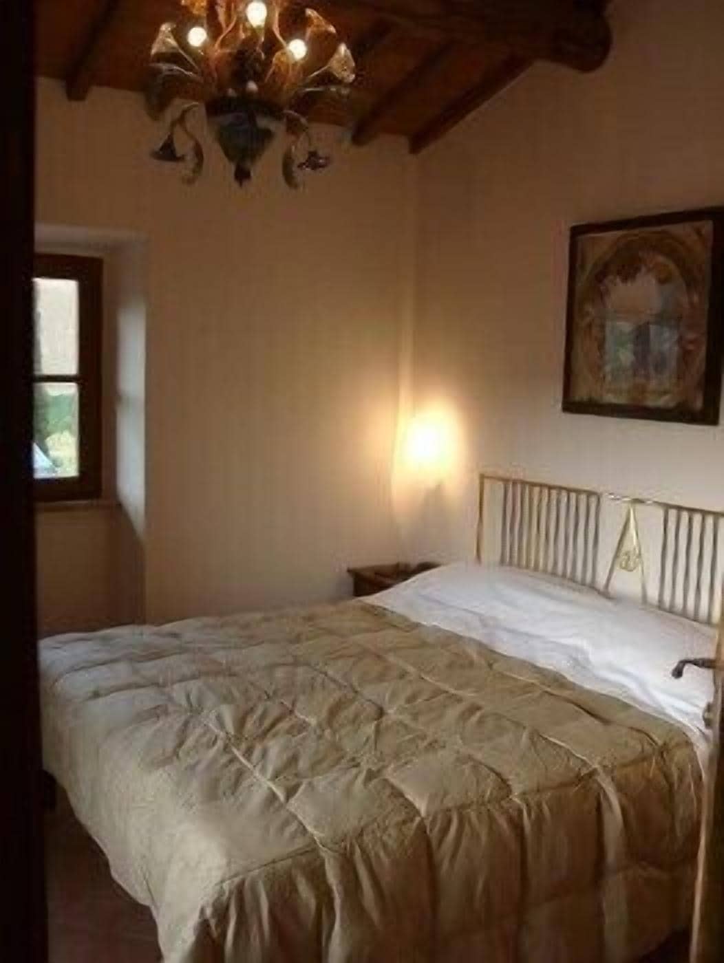 A bedroom with a bed, a chandelier, a painting on the wall, and a window.