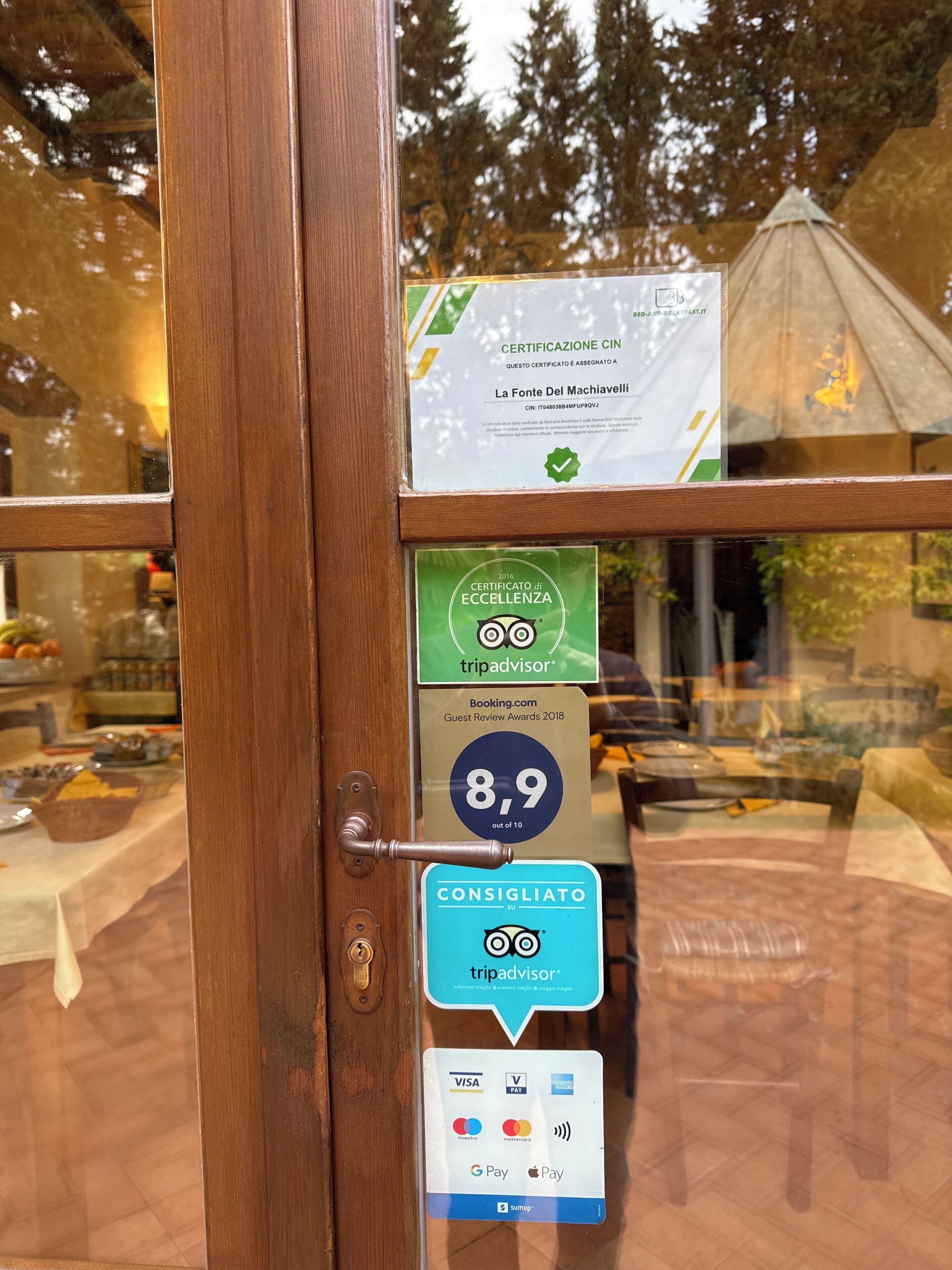 Une porte en bois avec un panneau de verre, un certificat, un badge TripAdvisor, un badge Booking.com et un lecteur de carte de paiement.