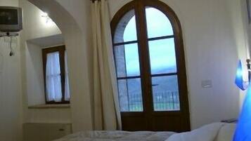 A bedroom with a bed, a window with curtains, a TV mounted on the wall, and a view of the outside.