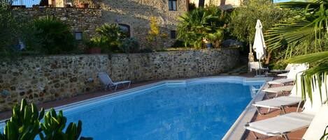 A stone building with a swimming pool and lounge chairs.
