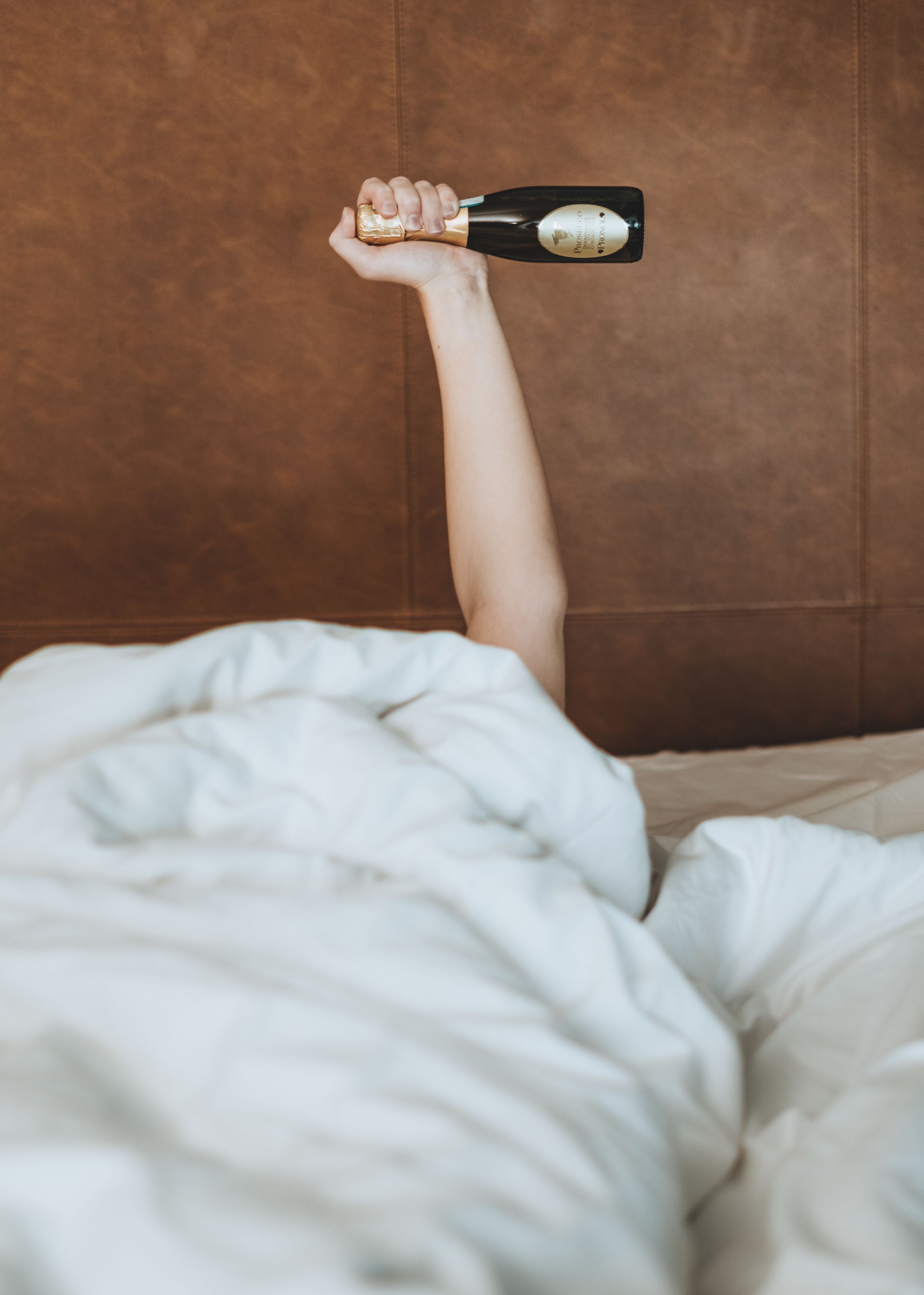 A person lying in bed with a bottle of champagne.