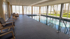 Ein geräumiger Poolbereich im Innenbereich mit freiem Blick ins Freie, eine Sitzecke mit Stühlen und eine sichtbare Treppe zu einer oberen Ebene.