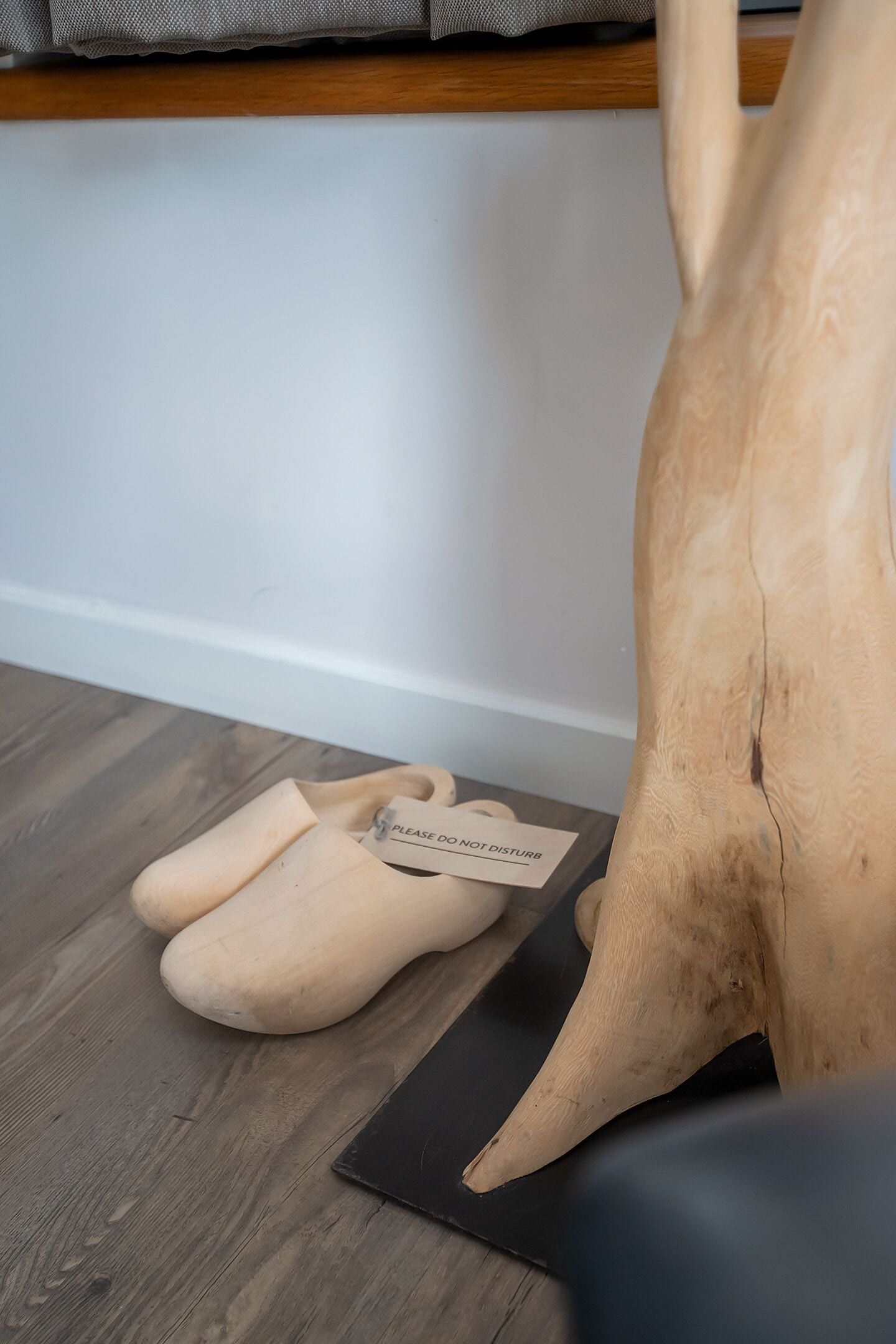 A wooden sculpture, a pair of beige slippers, and a black mat on a wooden floor.