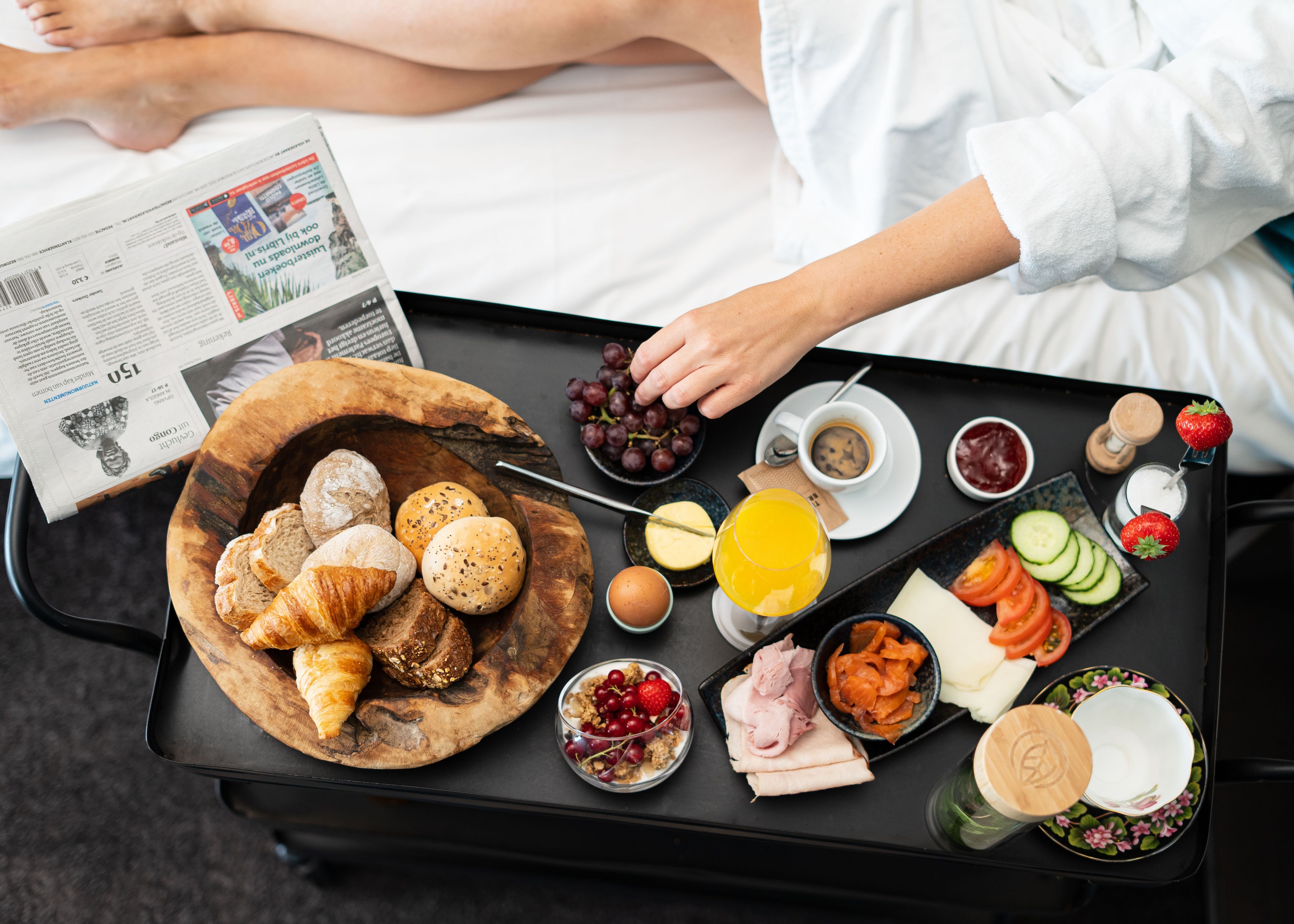 Bandeja de desayuno con cruasanes, panecillos, queso, jamón, huevos, uvas, zumo de naranja y diversas frutas y verduras.