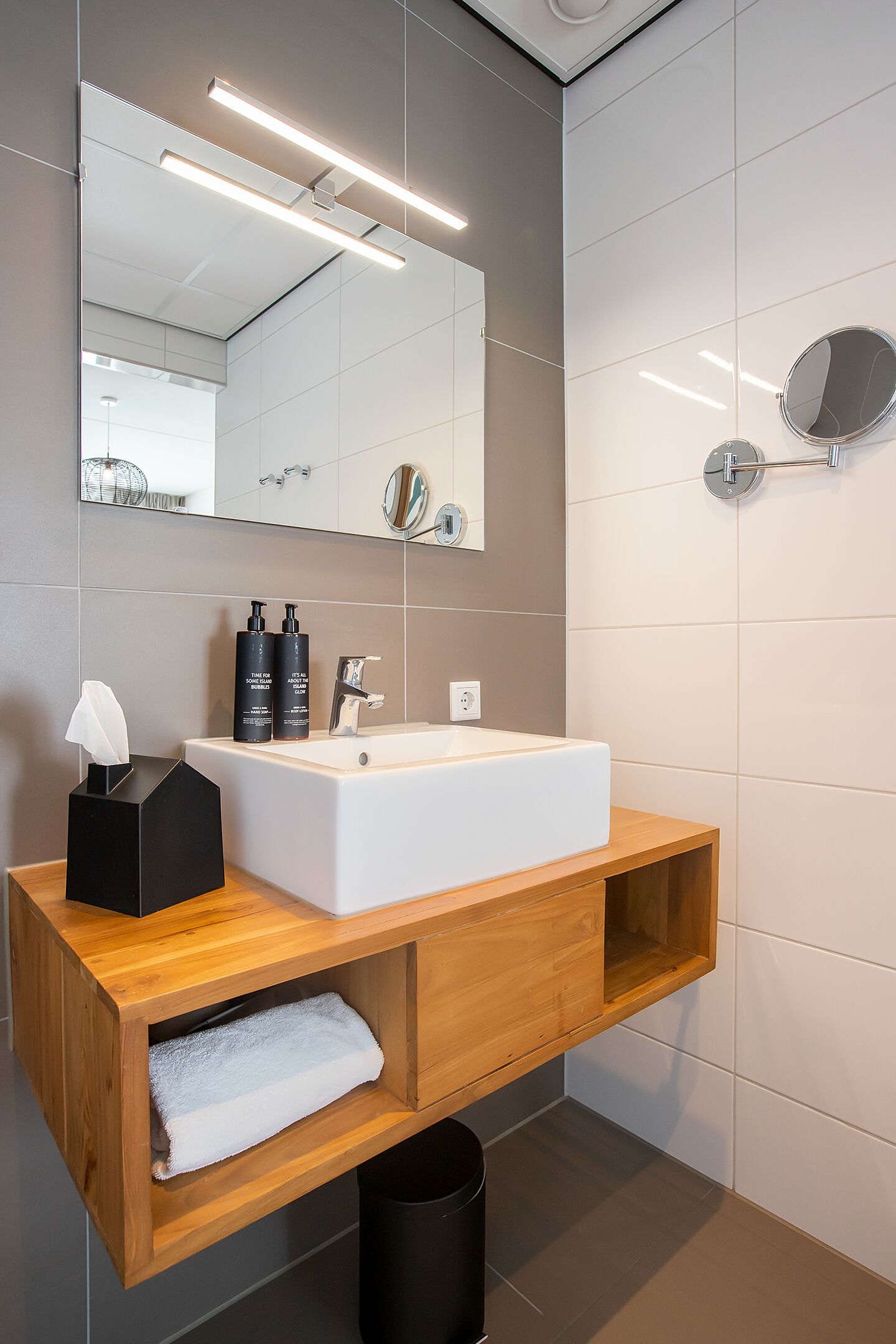 Un baño moderno con un lavamanos blanco, tocador de madera y un espejo grande.