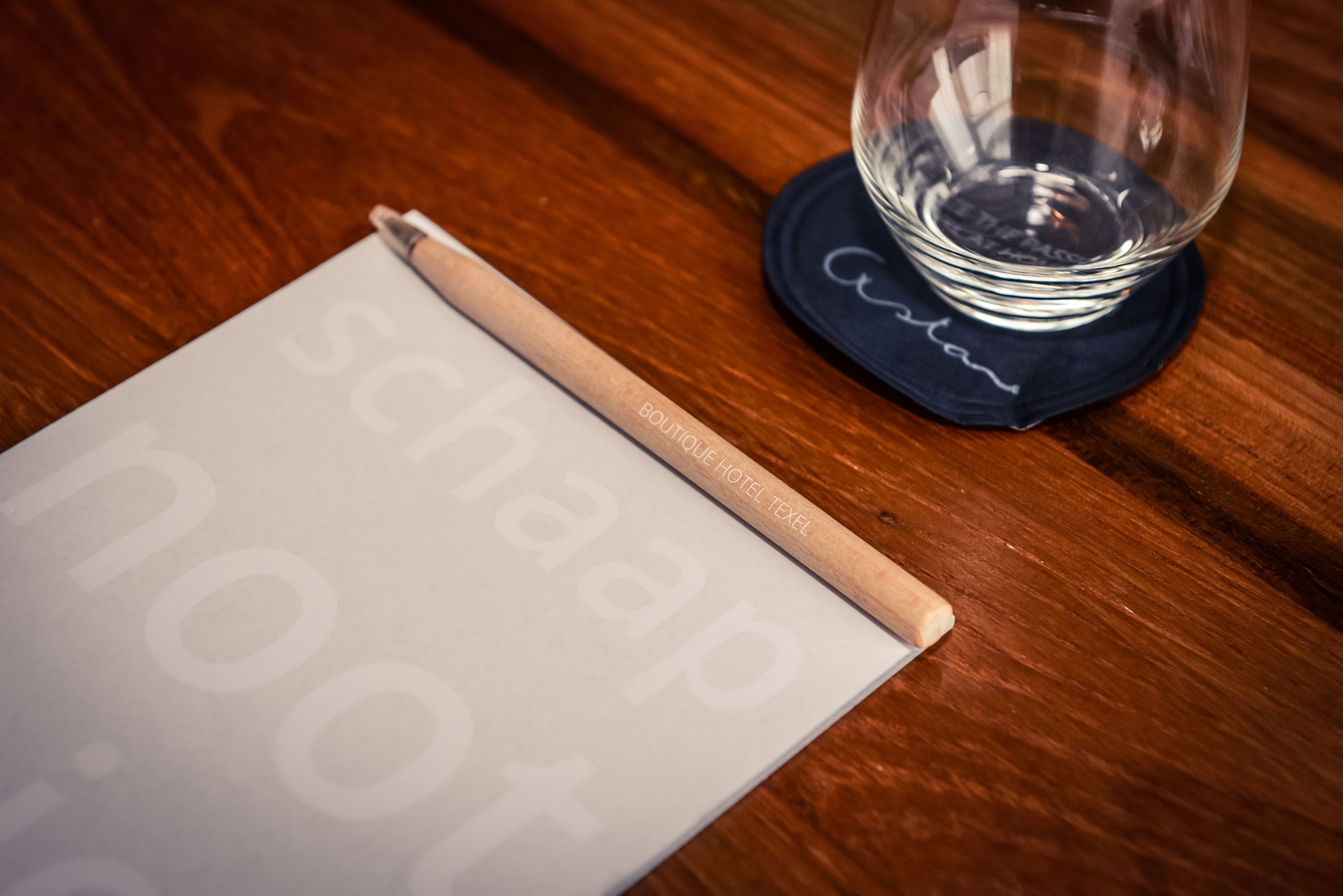 Een houten tafel met een notitieboek, een pen en een helder glas met een onderzetter.