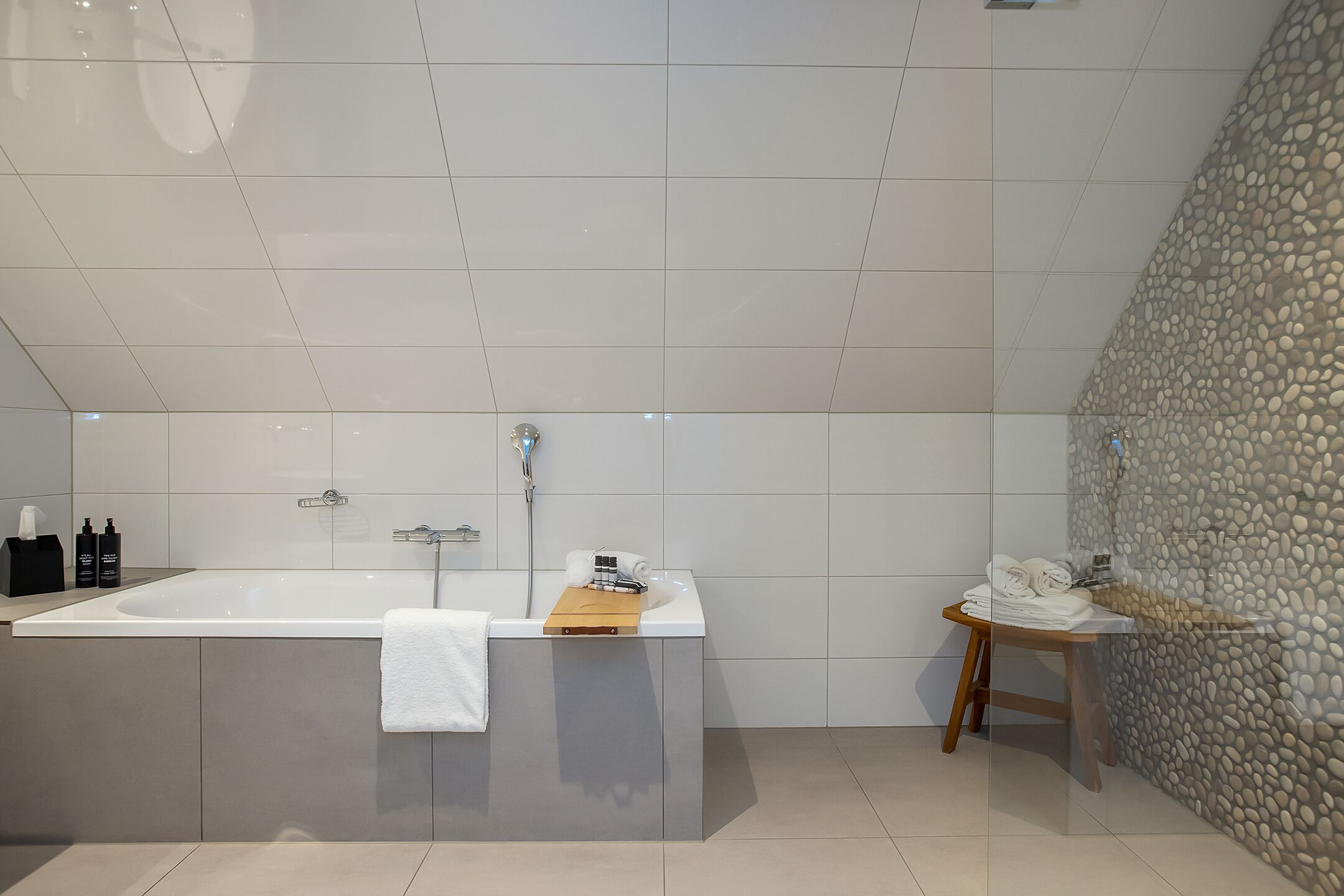 Ein modernes Badezimmer mit einer großen Badewanne, einem hölzernen Hocker und einem Handtuchhalter.