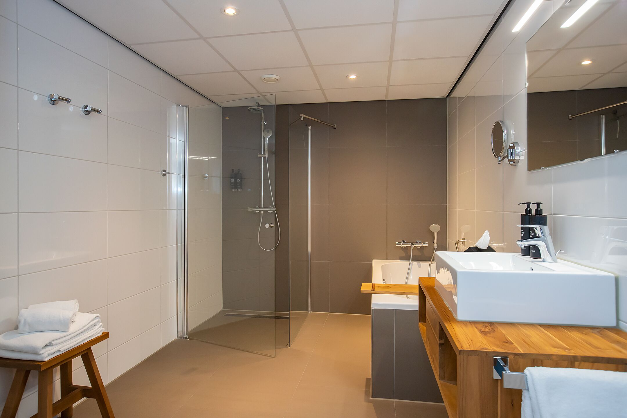 A modern bathroom with a glass shower enclosure, a wooden vanity, and a large mirror.