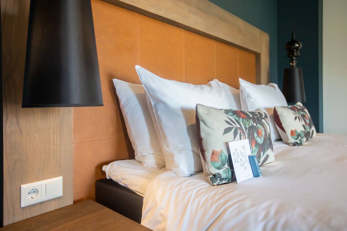 A neatly made bed with white and floral pillows, a wooden headboard, and a bedside table with a lamp.