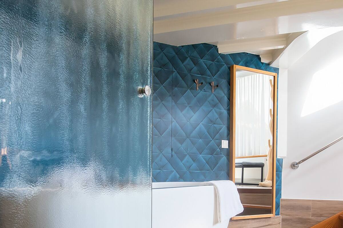 A modern bathroom with a glass-enclosed bathtub, a blue textured wall, and a wooden floor.