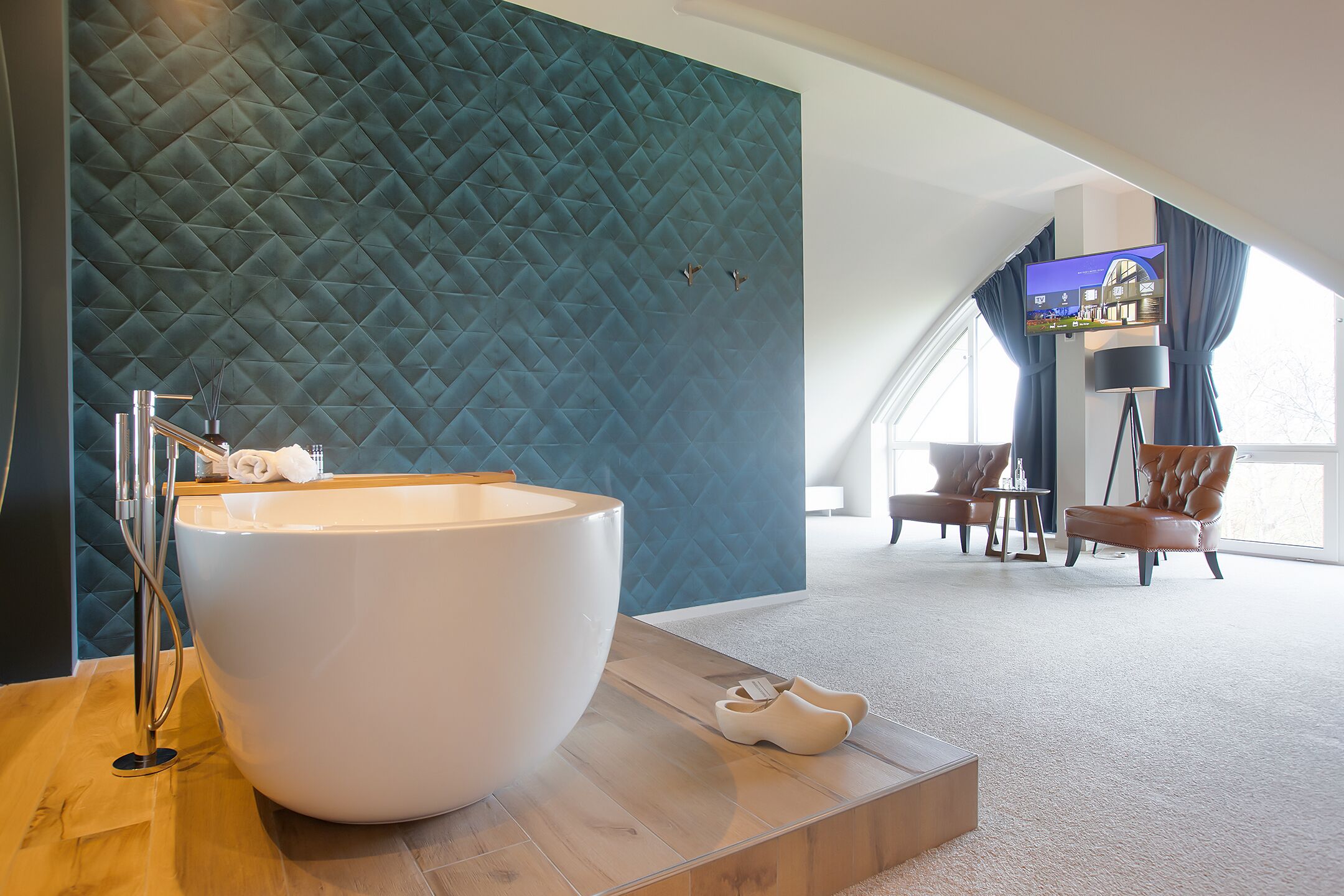 A modern bathroom with a large white bathtub, a wooden vanity, and a blue textured wall.