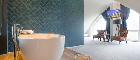 A modern bathroom with a large white bathtub, a wooden vanity, and a blue textured wall.