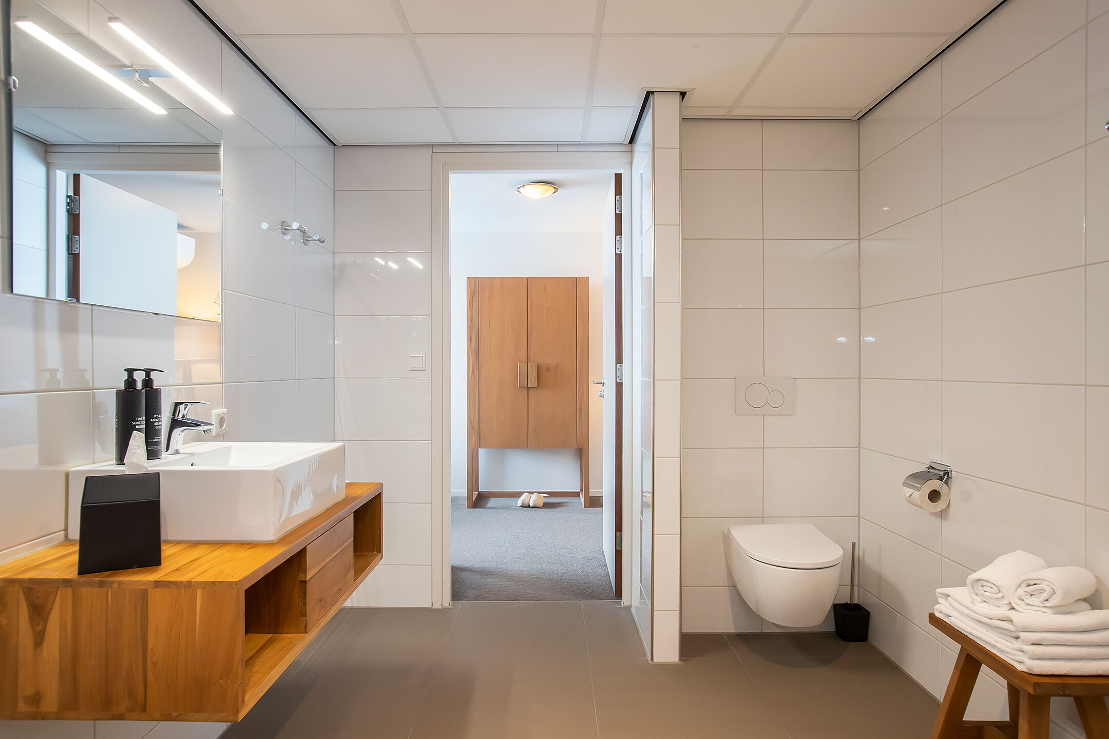 A modern bathroom with a wooden vanity, a large mirror, a white sink, and a toilet.