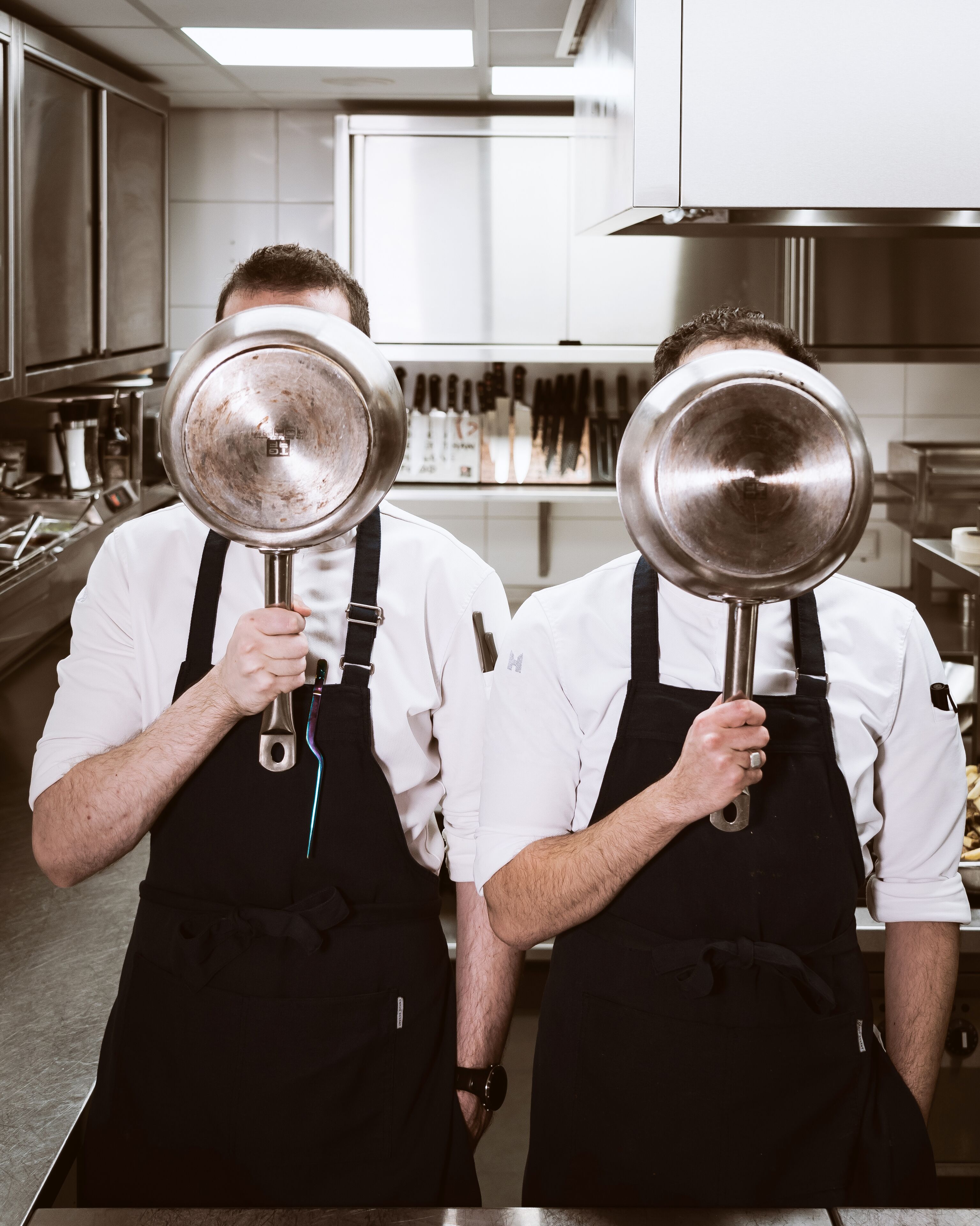 Dos cocineros en una cocina sosteniendo ollas grandes.