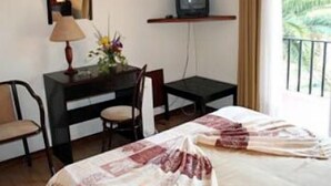 A hotel room with a bed, a desk with a chair, a television, and a window with a view of greenery. - Hotel João Capela (Aveiro)