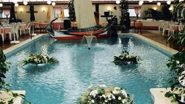 An indoor swimming pool with a sailboat decoration and floral arrangements. - Hotel João Capela (Aveiro)