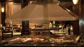 A buffet area with various food stations, a large overhead ventilation hood, and a warm, dimly lit interior. - Hotel João Capela (Aveiro)