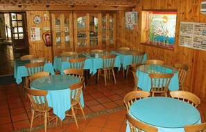 Un restaurante con paredes de madera, mesas y sillas azules. Hay vitrinas con alimentos y un extintor de incendios en la pared.