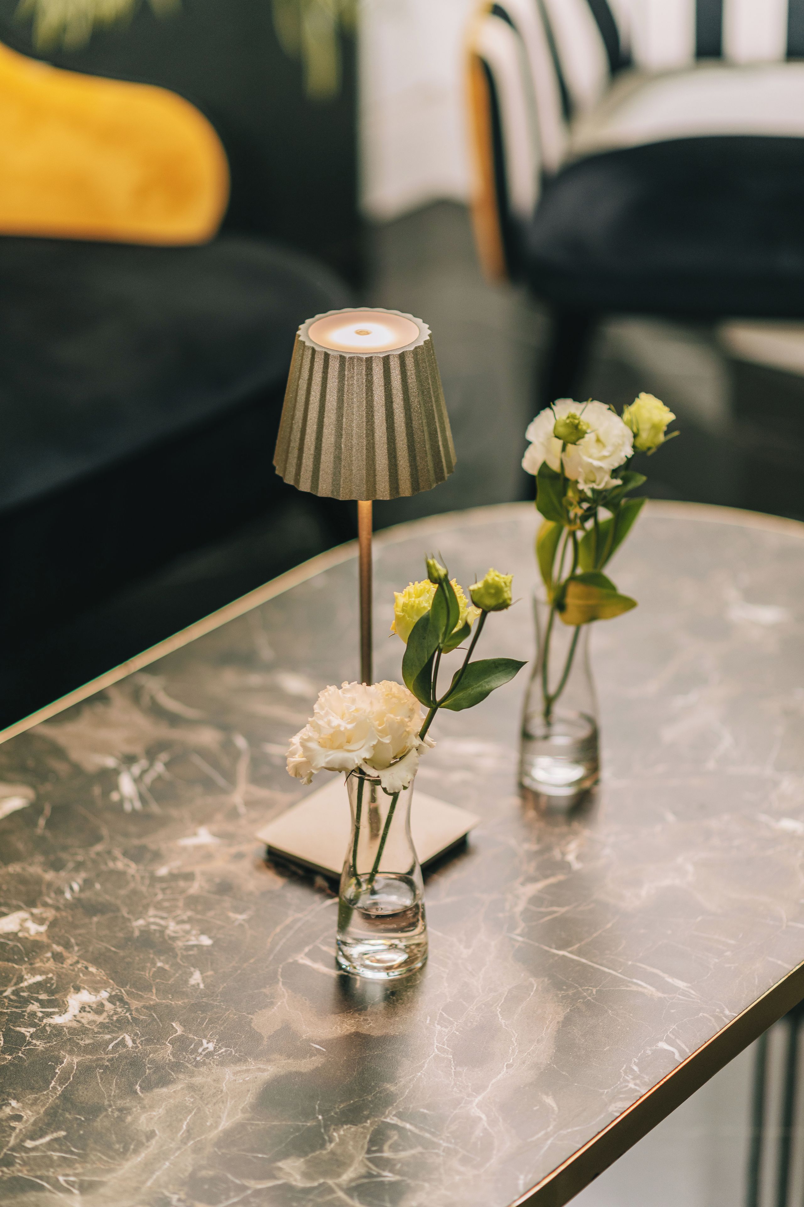 Une table en marbre, ornée de deux vases en verre contenant des fleurs et d’une lampe.