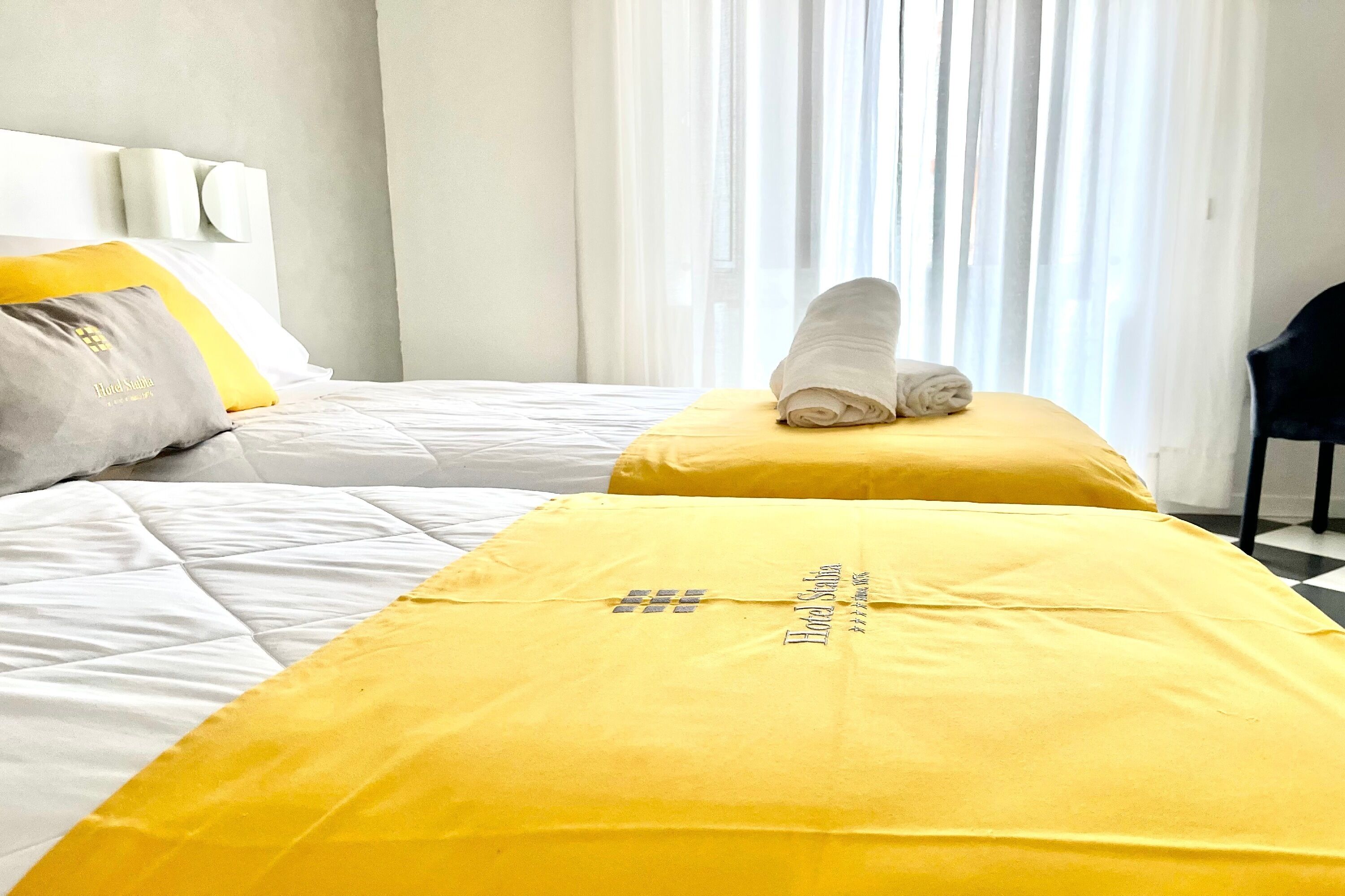 Habitación de hotel con dos camas, cada una con una colcha amarilla y una toalla enrollada en la cabecera.