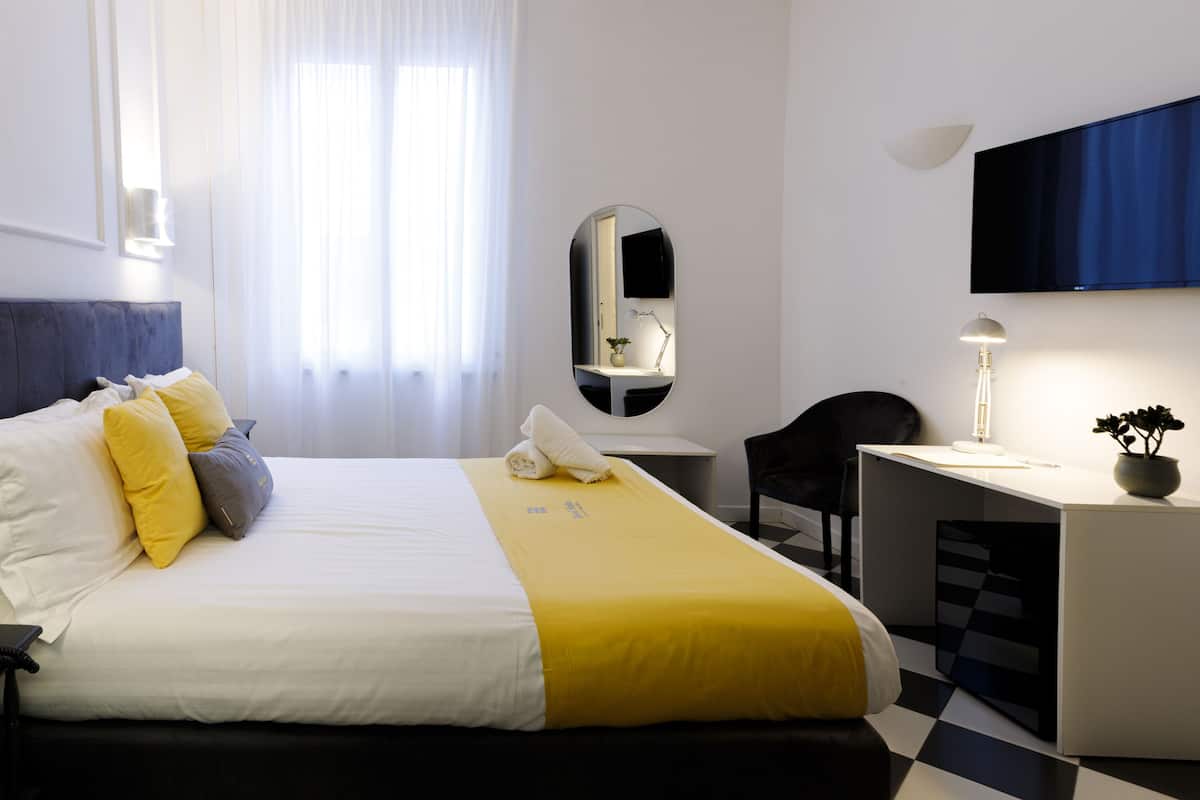 A hotel room with a bed, a desk, a chair, a TV, and a mirror.