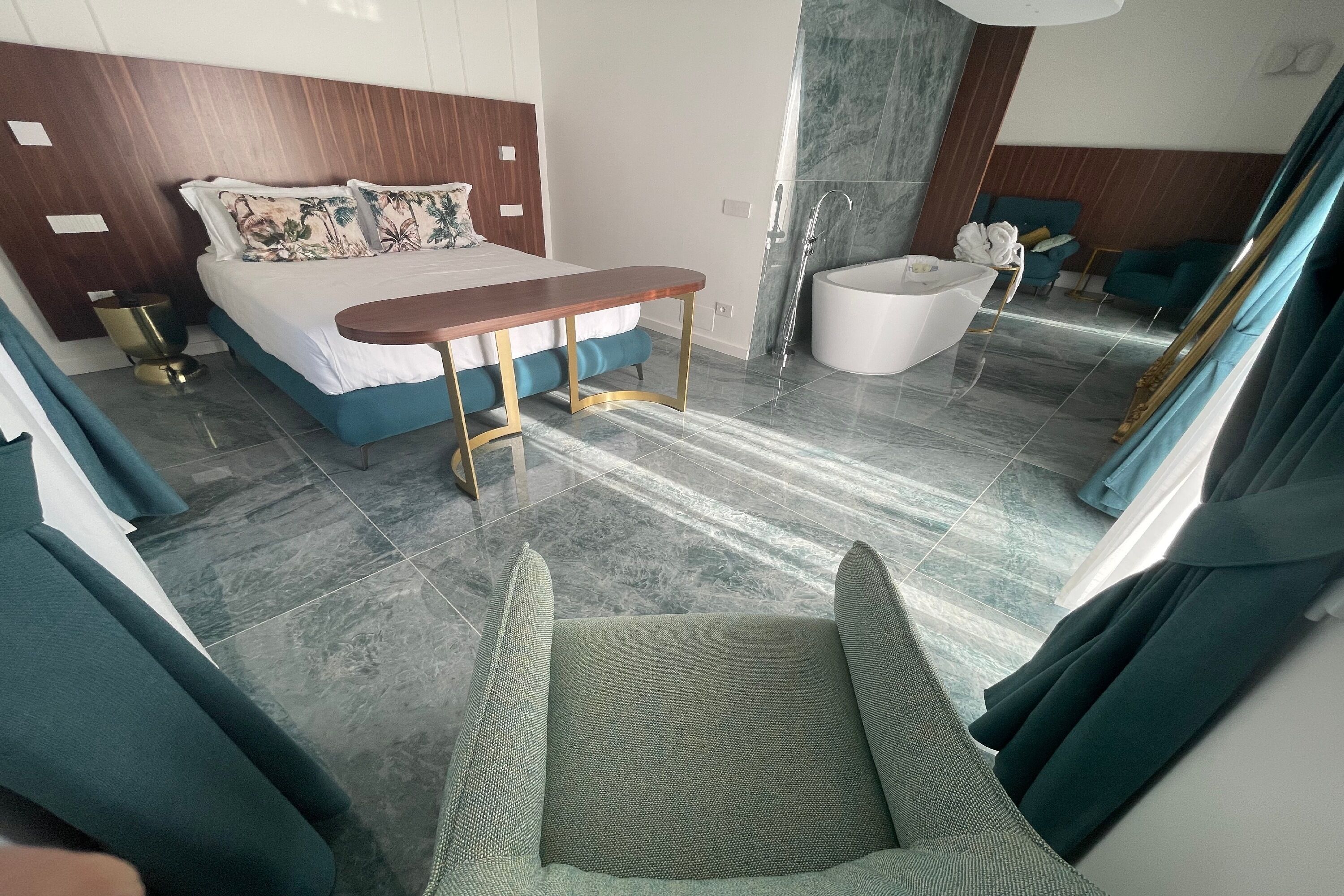 A modern hotel room with a bed, a small table, a chair, a bathtub, and a large mirror.