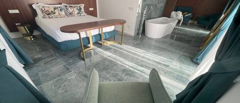 A modern hotel room with a bed, a small table, a chair, a bathtub, and a large mirror.