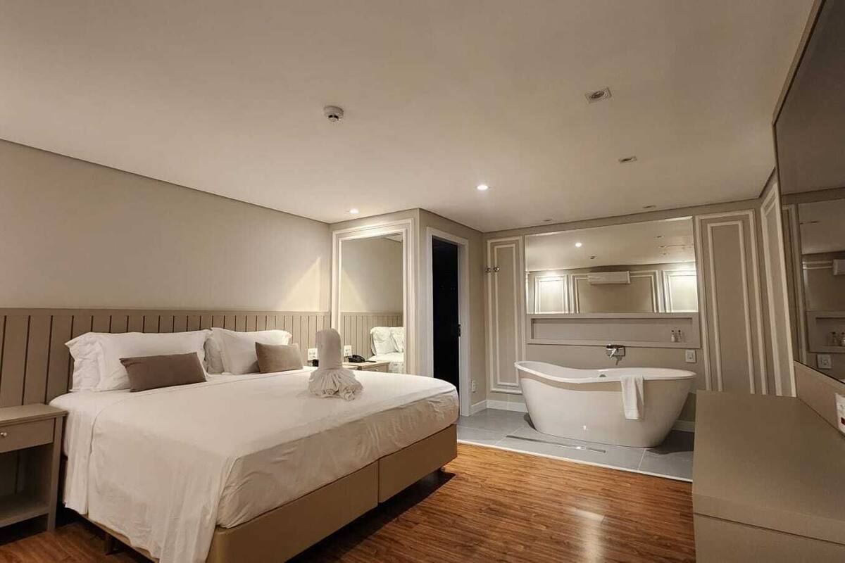 A modern hotel room with a large bed, a separate bathroom with a bathtub, and a walk-in closet.