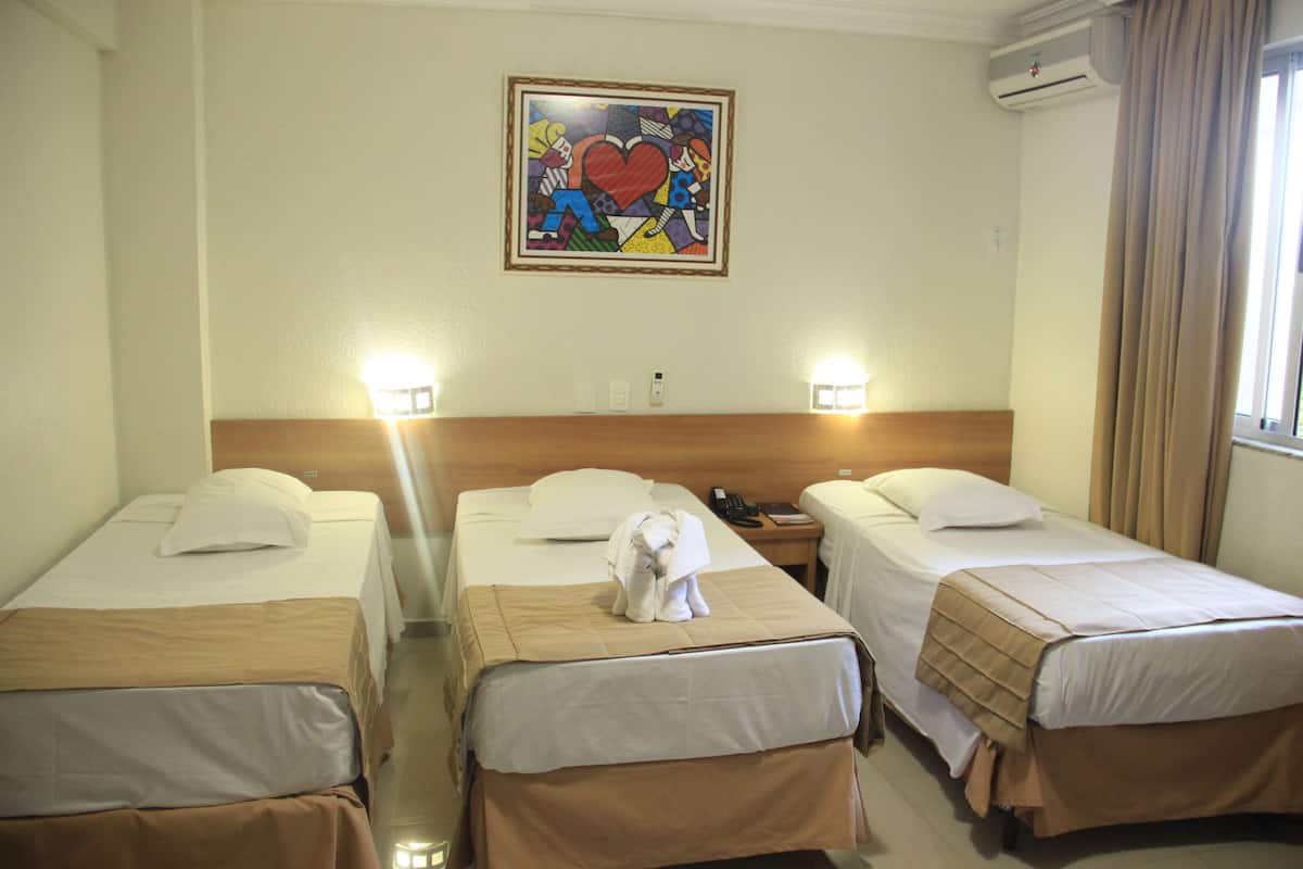 A hotel room with two single beds, a wooden headboard, a painting of a heart, and an air conditioning unit.