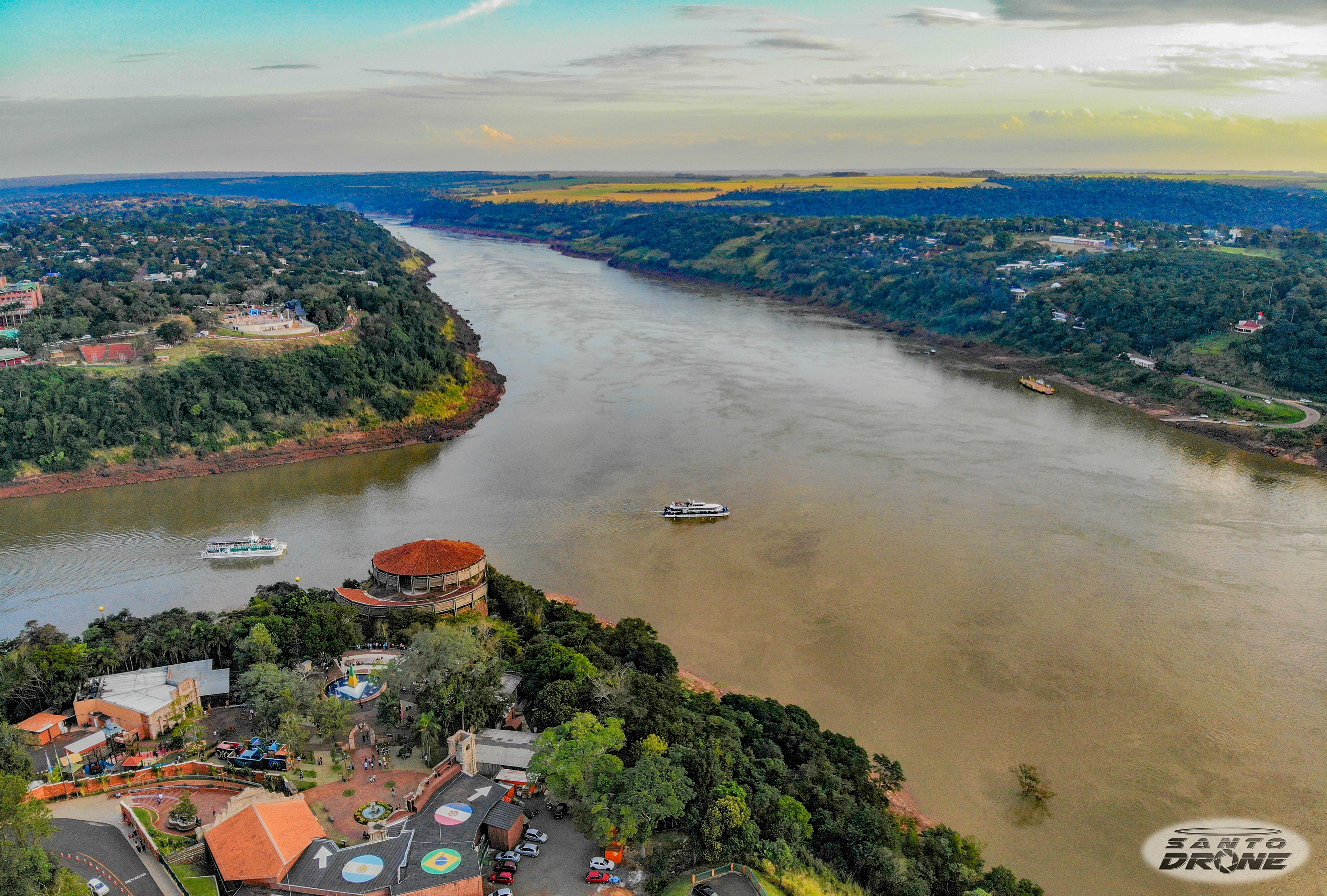An aerial view of a riverside area with a boat dock, buildings, and greenery.