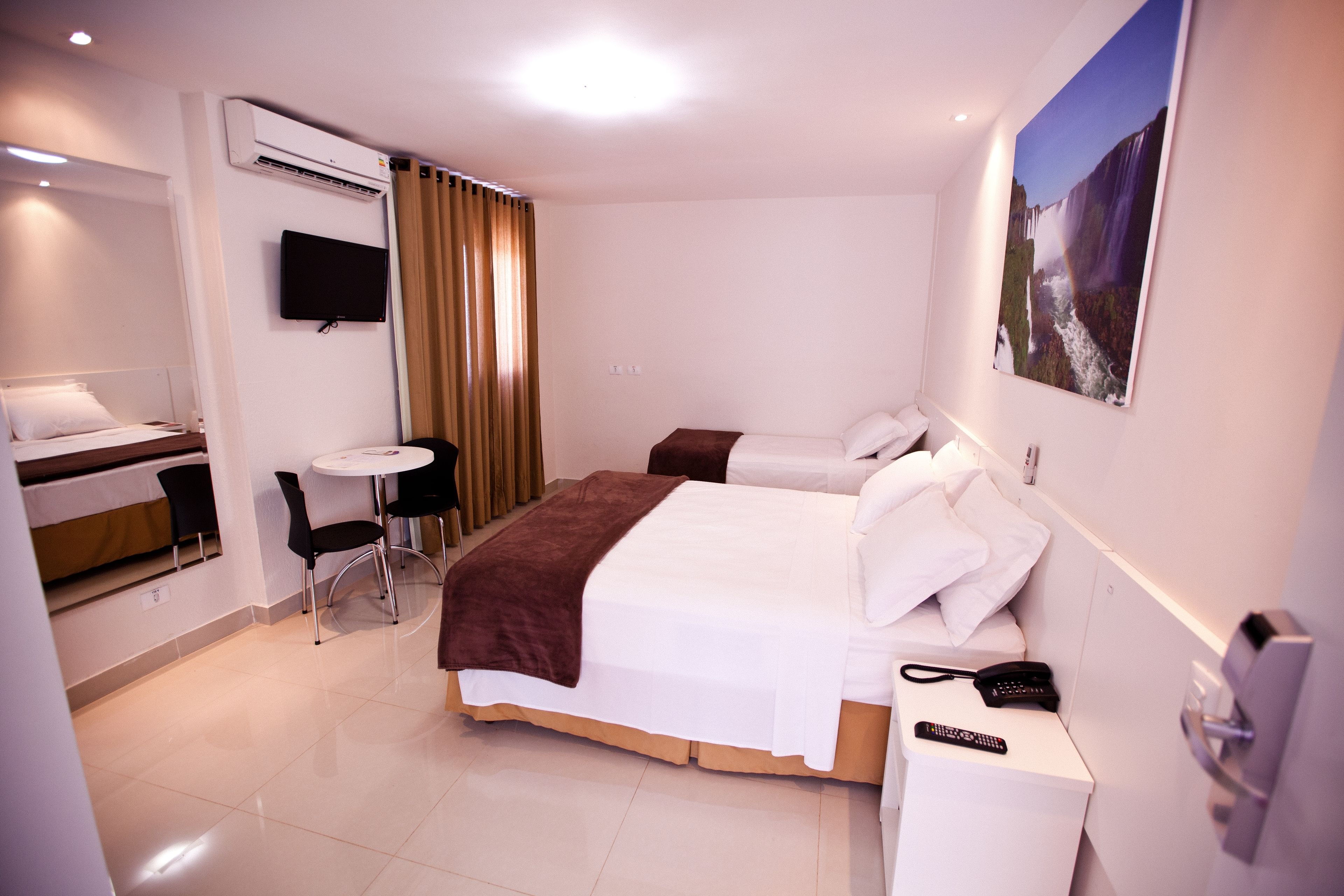 Ein Hotelzimmer mit Bett, Nachttisch, Stuhl, Fernseher und einem Bild an der Wand.