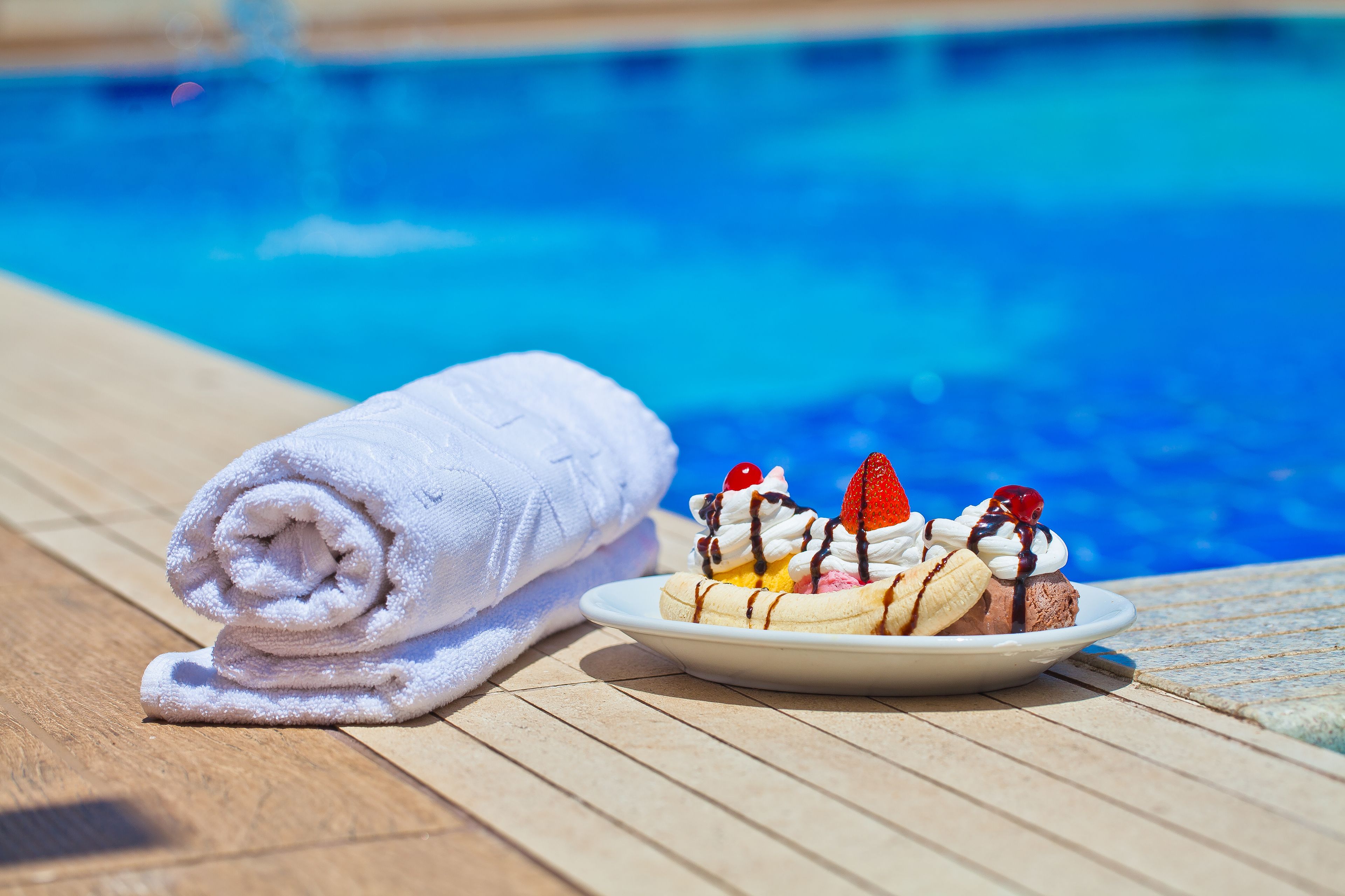 Une terrasse en bois avec une serviette blanche et une assiette de desserts, près d’une piscine.