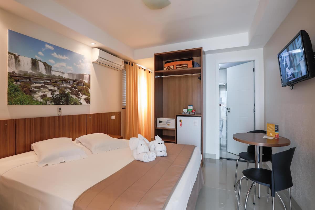 A hotel room with a bed, a desk, a chair, a television, a wardrobe, and a painting on the wall.