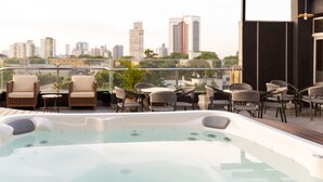 A rooftop terrace with a hot tub, wicker chairs, and tables, overlooking a cityscape. - Del Rey Quality Hotel (Foz do Iguaçu)