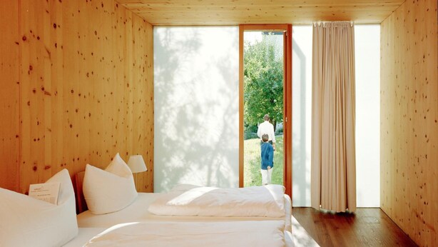 A bedroom with two beds, wooden walls, and a large sliding glass door leading to an outdoor area. - Hörger Biohotel und Tafernwirtschaft (Kranzberg)