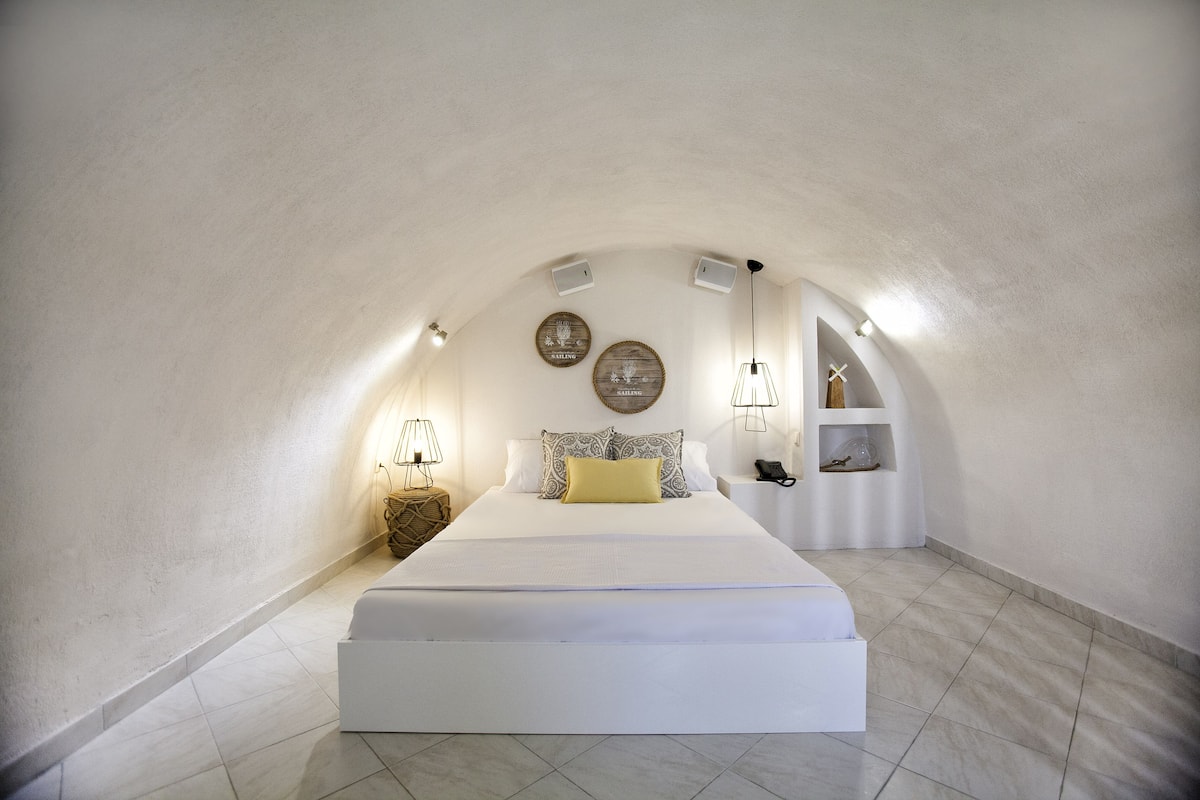 Une chambre à coucher avec un grand lit, une table de chevet, une lampe et une petite étagère sur laquelle se trouvent un téléphone et quelques objets décoratifs.