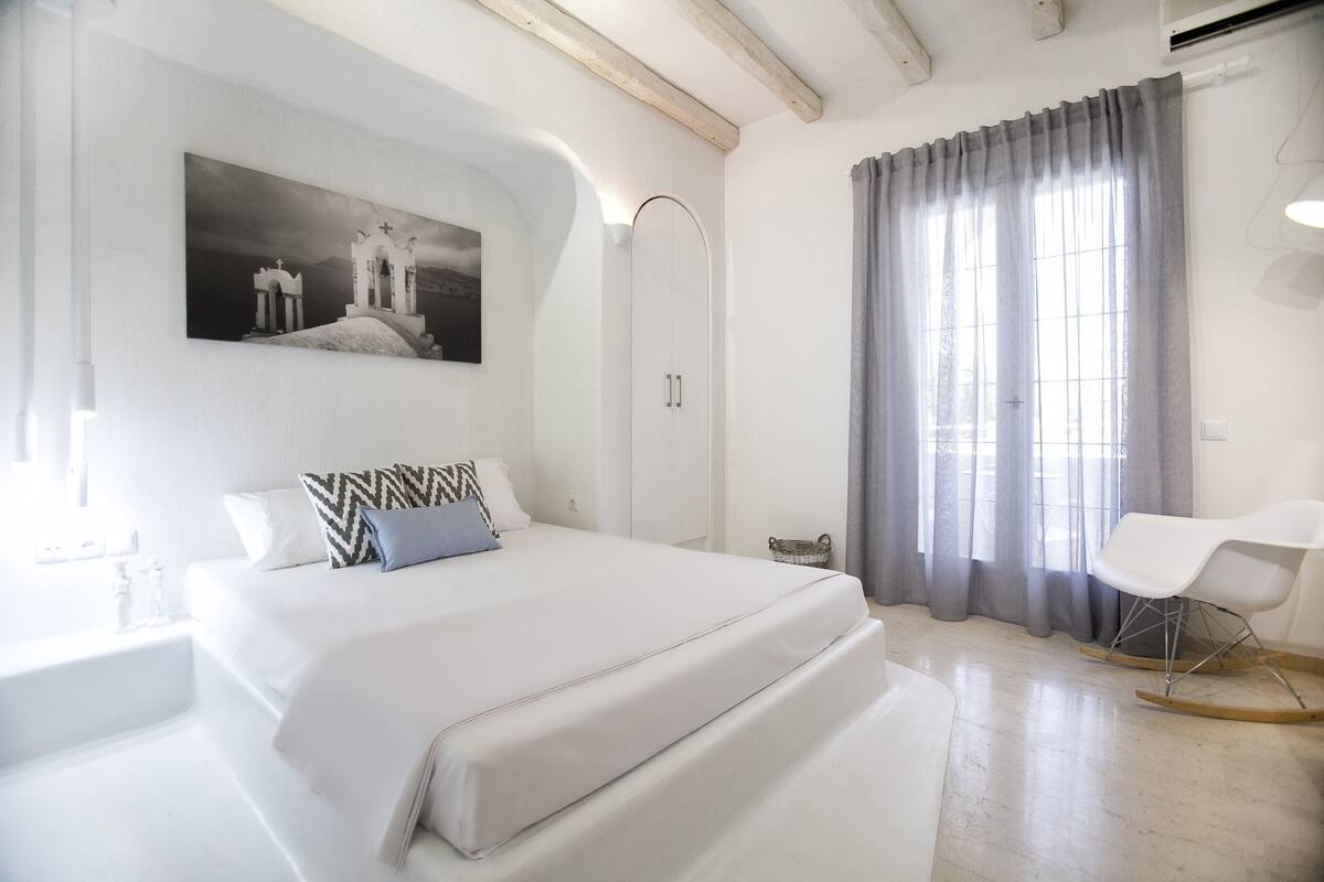 Une chambre d’hôtel moderne avec un grand lit, une armoire, un fauteuil à bascule et un tableau au mur.