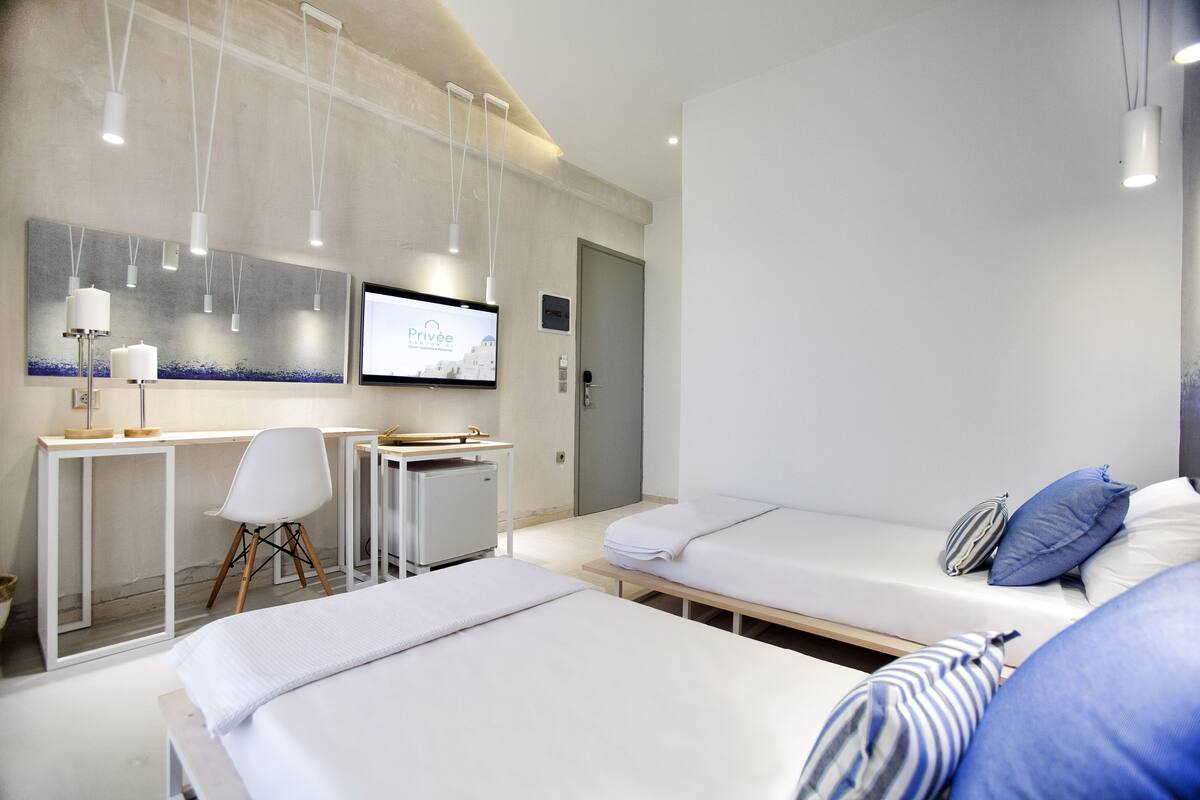 Une chambre d’hôtel moderne avec deux lits, un bureau, une chaise et un téléviseur diffusant le programme « Privée ».