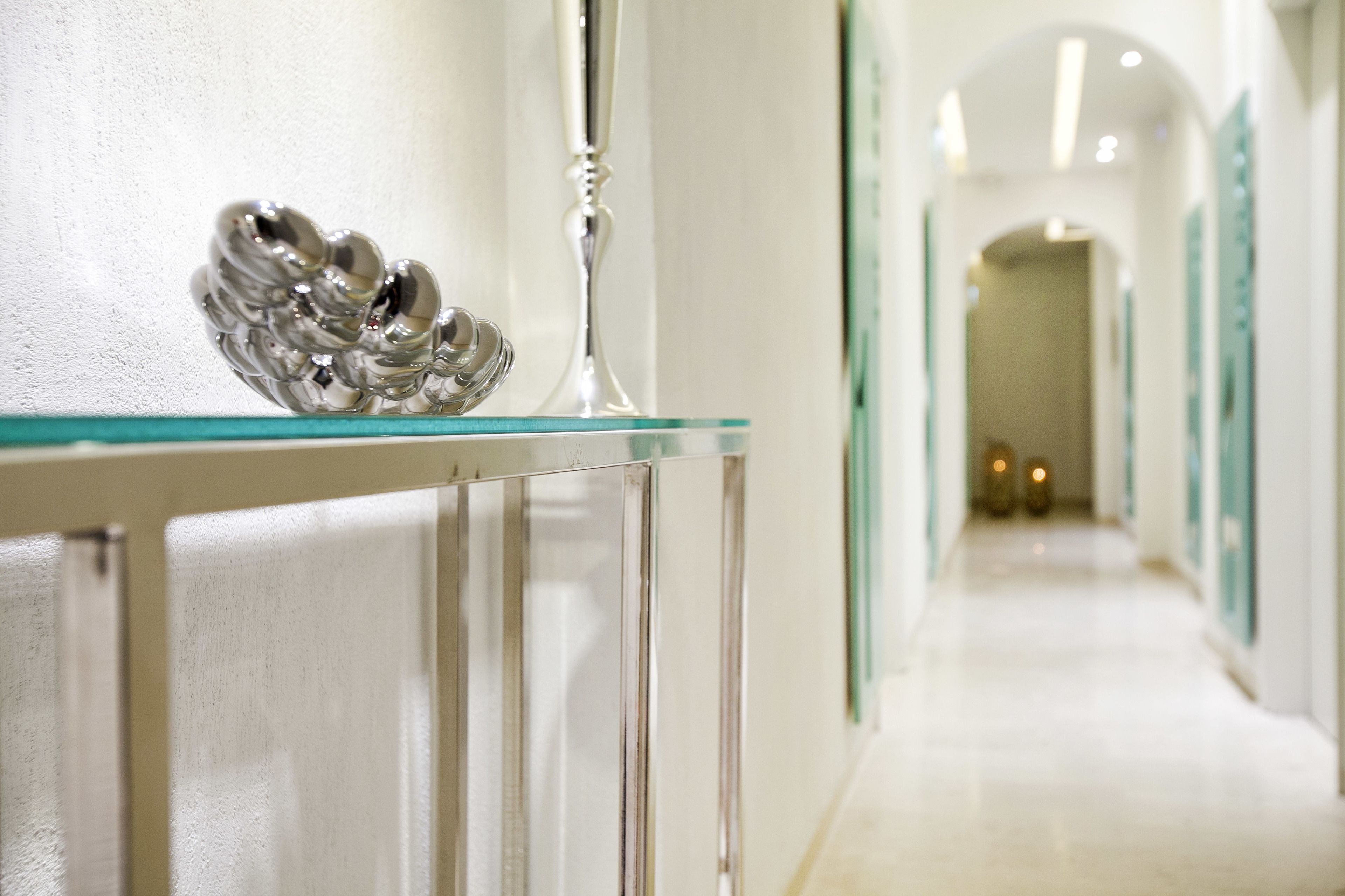 Un couloir doté d’une rambarde en verre, d’un élément décoratif en métal et d’un grand vase élancé.