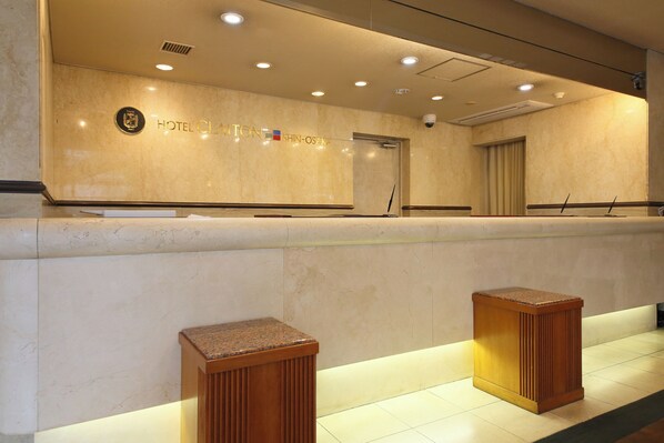 A hotel reception area with a marble counter, a reception desk, and two wooden stools.