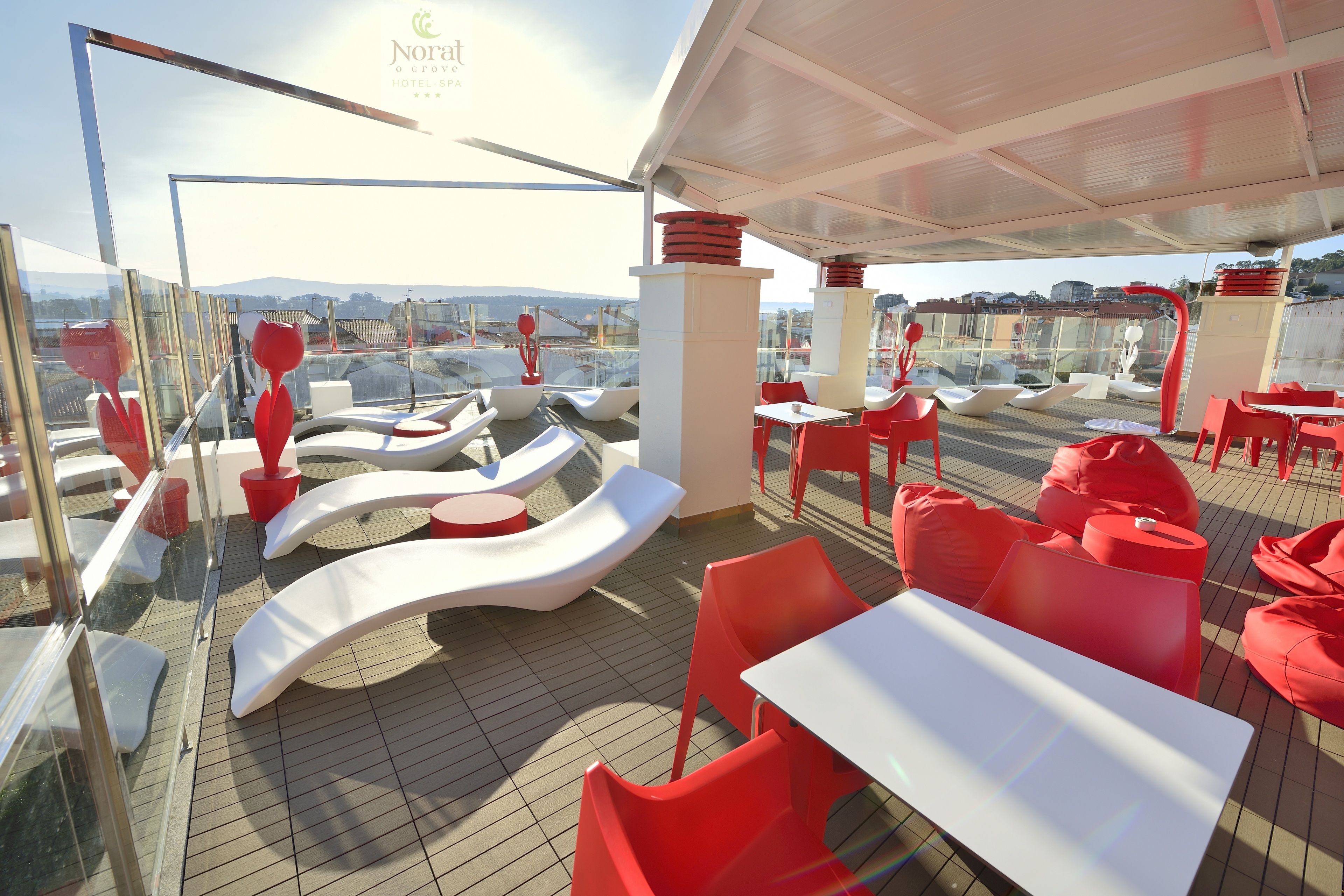 A rooftop terrace with red and white seating, a glass balustrade, and a view of the cityscape.