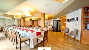Een restaurantgedeelte van een hotel met lange tafels gedekt voor meerdere gasten, houten stoelen en een warme, sfeervolle verlichting.