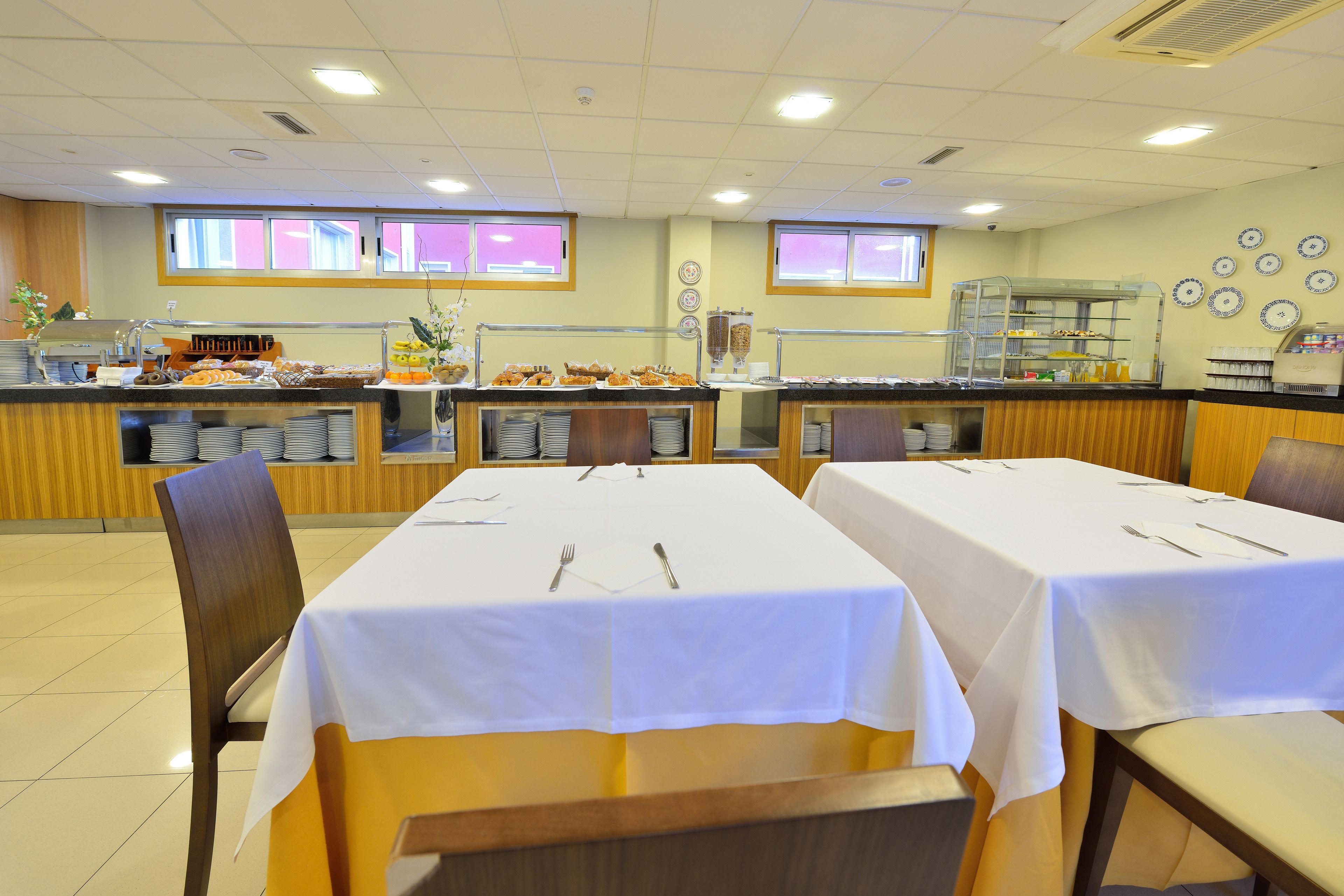 A dining area with tables set for service, a buffet with various food items, and a counter with a beverage dispenser.