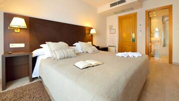 Habitación de hotel con una cama grande, dos mesitas de noche, un tablero de noche, un cabecero de madera y un baño visible a través de una puerta abierta.